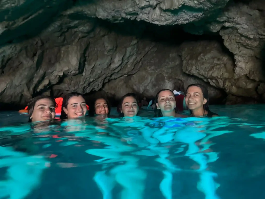 Group of smiling women swimming inside the glowing Blue Cave near Dubrovnik, Croatia, surrounded by turquoise water and rocky cave walls