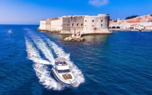 Luxury yacht cruising past Dubrovnik Old Town fortress on a sunny day in the Adriatic Sea